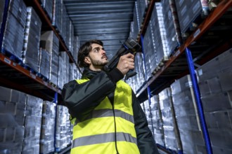 Man wearing a safety vest and jacket scanning product pallets stored on high shelves in a cold or