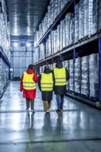 Workers wearing safety vests walking down an aisle in a cold storage warehouse, inspecting pallets