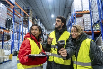 Diverse team of warehouse workers wearing safety vests and warm clothing, using a barcode scanner
