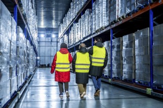 Three workers wearing safety vests and warm clothing are inspecting goods in a modern industrial