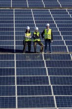 Team of diverse engineers with hard hats and safety vests standing confidently on a large solar