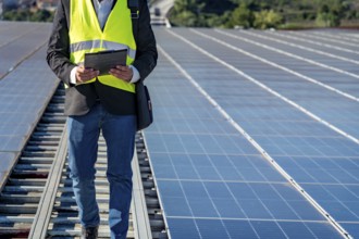 Technician working on a large solar panel installation, reviewing data on a clipboard while walking