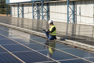 Male engineer checking solar panel efficiency on a large factory rooftop after installation,