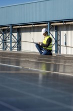 Male engineer wearing a hard hat and safety vest performing an inspection of rooftop solar panels