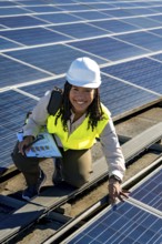 Young woman engineer with safety helmet and vest, smiling while inspecting photovoltaic panels