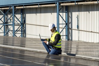 Male engineer inspecting and maintaining solar panel installation on a factory rooftop, capturing