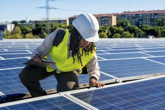 Woman engineer in safety hard hat and vest inspecting photovoltaic solar panels on a commercial