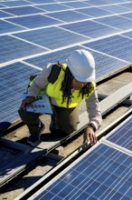 Woman engineer in a hard hat and safety vest inspecting solar panels on a rooftop, working on