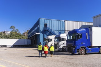 Logistics workers in high visibility vests walking past semi trucks parked at the loading docks of