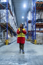 Woman wearing warm jacket and safety vest scanning inventory with a barcode reader, managing stock