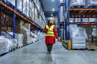 Female warehouse worker wearing warm clothing and a safety vest, scanning inventory while walking