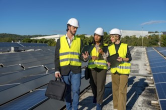 Team of diverse energy engineers and technicians inspecting solar panels on a rooftop, discussing