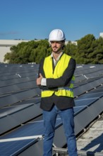 Engineer wearing a hard hat and safety vest standing confidently with arms crossed on a rooftop