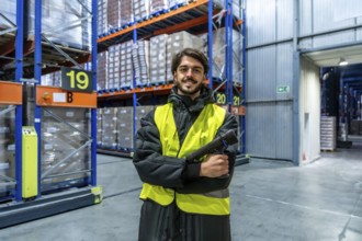 Man in safety vest and warm clothing holding a scanner, working in a cold storage warehouse with