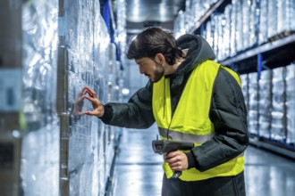 Warehouse worker in protective cold weather gear and safety vest inspecting a stack of frozen goods