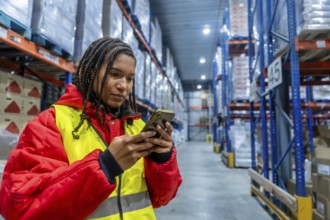 Female warehouse worker wearing warm clothing and a safety vest, actively managing inventory and