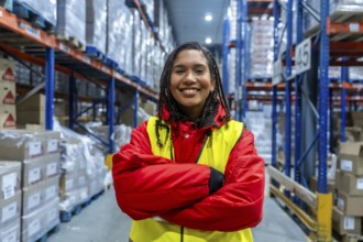 Smiling young woman standing with arms crossed in a brightly lit cold storage warehouse. Wearing
