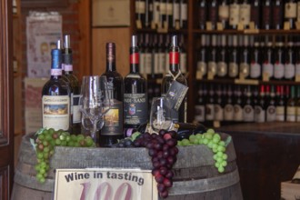 Cosy wine shop with wine bottles, glasses and grapes on a wooden barrel, Tuscany, Italy