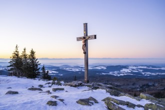 Christian cross on the peak of Mount Lusen with the view over the hills of the bavarian forest at