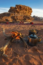 Two teapots next to an open fire in desert sand, eroded rocks in the background, Wadi Rum, Jordan