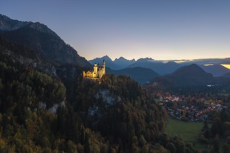 Illuminated Neuschwanstein Castle on hills, surrounded by imposing mountains and an evening