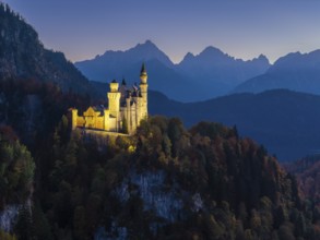 Sublime illuminated Neuschwanstein Castle on a ridge in the midst of an alpine landscape at sunset,