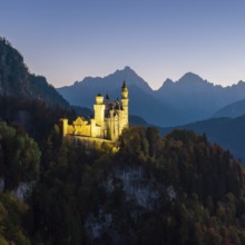 Illuminated Neuschwanstein Castle at dusk against a mountain backdrop, Schwangau near Füssen,