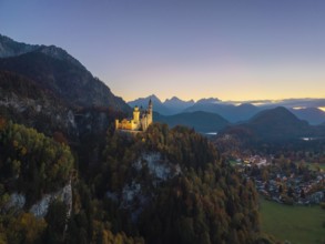 Neuschwanstein Castle stands illuminated on a hill, surrounded by mountains and a natural panorama,