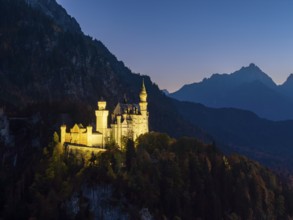 Mysterious view of Neuschwanstein Castle at dusk with mountains in the background