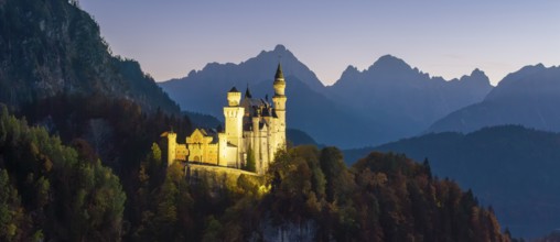 Wide-angle view of Neuschwanstein Castle at dusk and mountains in the background