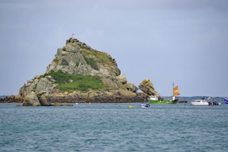 Rocky island with cross and green boat in calm sea under blue sky, Isles of Scilly, Cornwall,