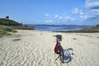 Bicycle on empty sandy beach with views of calm sea under clear skies, St Agnes, Isles of Scilly,