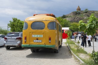An orange bus from behind, parked next to a busy street with people and buildings, PAZ-672, minibus
