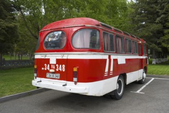 Back view of a red vintage bus in a parking lot with trees in the background, PAZ-672, minibus of