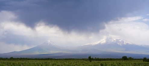 Two snow-capped mountains under dramatic skies with dark clouds over vast fields, Ararat and Little