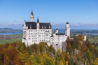 The nearby Neuschwanstein Castle stands majestically above autumn trees and blue horizons,