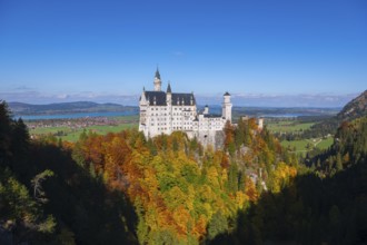 The magnificent Neuschwanstein Castle surrounded by autumn colors and vast green hills, Schwangau,