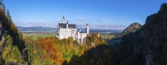 Neuschwanstein Castle towers over colorful forests in a vast landscape with blue skies, Schwangau,