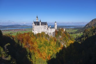 The magnificent Neuschwanstein Castle towers over an autumnal landscape with wide skies, Schwangau,