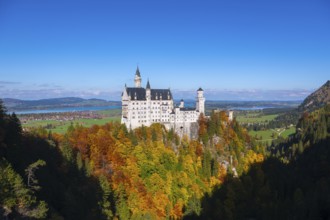 The picturesque Neuschwanstein Castle overlooks colorful autumn forests under clear skies,