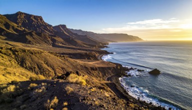 Desert landscape converges with ocean along a rugged coastal area, shore break at cliffs, blue