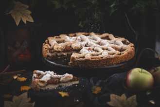 Icing sugar falls on apple pie surrounded by autumn leaves in a dark environment