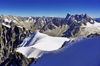 Mountaineers climb over a snow-covered ridge with Grandes Jorasses mountain in the background,
