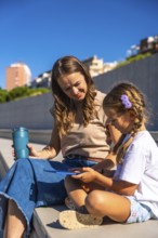 Mother and daughter smiling, sitting together on steps enjoying time outdoors, holding a reusable