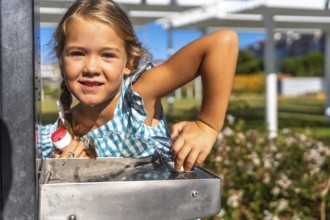 Young child refreshing herself with a drink of water from a public fountain in a sunny park,