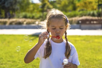 Little girl enjoying outdoor activity, blowing iridescent soap bubbles, experiencing joy and