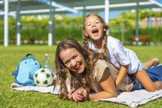 Mother and daughter bonding and having fun at a picnic in the park, the child playfully riding on