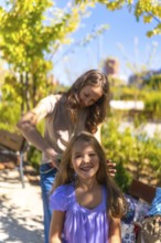 Mother is combing her daughter's long hair with a comb while the happy girl is looking at the