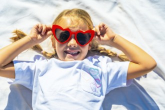 Young child lying outdoors on a white blanket, expressing joy and playing with vibrant red heart