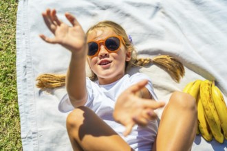 Young happy girl relaxing on a white blanket in the grass, wearing orange sunglasses and white t